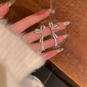 Close-up of sparkling silver bow earrings with zircon stones held on a finger