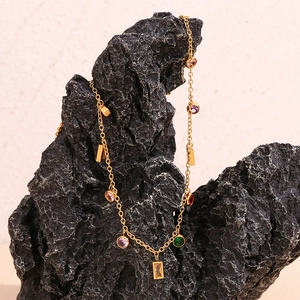 Close-up of 18K gold plated chain necklace with colorful gemstones on black rock