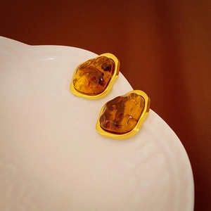 Macro shot of geometric irregular amber resin stud earrings with matte gold frames