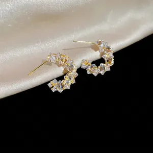 Sparkling C-shaped geometric hoop earrings with cubic zirconia on champagne silk backdrop