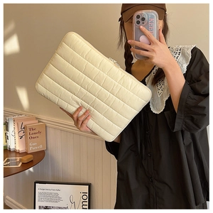 Lifestyle shot of quilted off-white laptop sleeve with stitched horizontal texture in cozy room