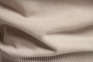 Macro detail of the beige knitted cotton sweater fabric showing soft texture and fine weave
