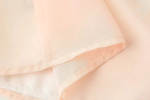 Détail du tissu en mousseline rose clair montrant une couture délicate et texture
