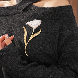 Close-up of a tulip brooch with textured silver petals and gold stem on grey knit