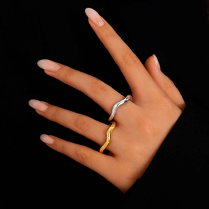 Polished gold and silver wave rings stacked on finger against a black background