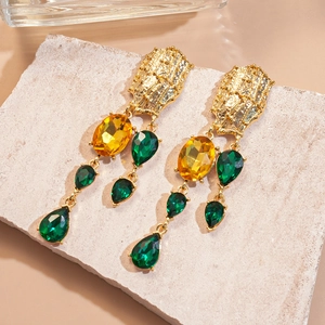 Detail of vintage gold drop earrings with emerald crystals on natural stone background
