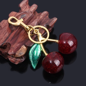 Detailed macro view of glittery red cherry keychain with green leaf and golden metal clasp