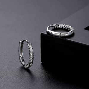 Silver oval hoop earrings with sparkling micro-pave crystals on a black textured background