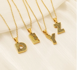 Détail macro de pendentifs lettres D, E, Y, Z en acier doré avec une texture gaufrée raffinée