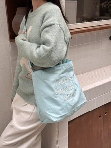 Close-up of light blue canvas tote bag featuring white embroidered dream quote and detail