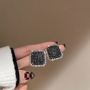 Detailed view of square houndstooth stud earrings with crystals held in hand