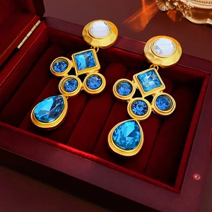 Macro view of vintage gold earrings with blue and white crystals in a red velvet box