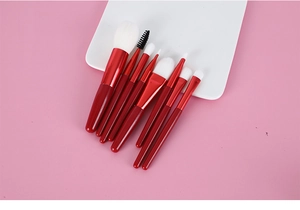 Flat lay of 8 mini makeup brushes with red handles and soft white fiber bristles on white tray