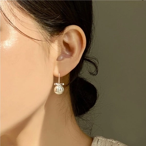 Detail of silver bowknot earrings with pearls worn by a model in soft lighting