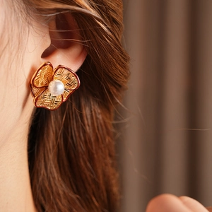 Close-up of gold flower earrings with red accents and white pearl on a model's ear