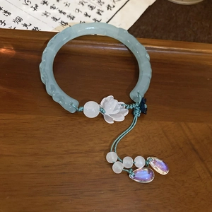 Détail d'un bracelet ouvert en imitation jade vert pâle avec charm lotus et pompon