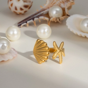 Vue détaillée d'une bague dorée avec étoile de mer et coquillage sur décor de plage