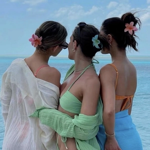 Three women on a beach wearing colorful frangipani flower hair claws with beachwear