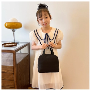 Girl carrying a black thermal fabric lunch bag in a home setting for kids' daily use