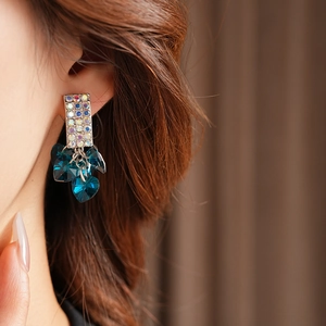 Close-up of dangling heart earrings with blue crystals and sparkling silver tassels