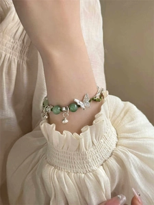 Detail of silver butterfly pendant and green beads on a bamboo-style woven bracelet