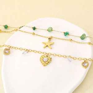 Close-up of gold-plated layering anklets with green jade beads, starfish and heart charms