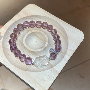 Detail of purple amethyst beaded bracelet with clear beast charm on wood tray
