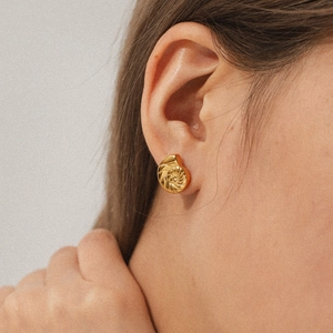 Close-up of golden shell-shaped stud earring worn by model in 18K gold plated steel