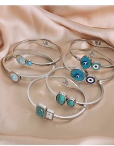 Close-up of polished silver steel bangles with turquoise, shell, and evil eye inlays