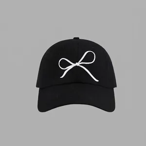 Close-up of white bow embroidery detail on a premium black cotton baseball cap