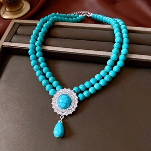 Close-up of double-layer turquoise beaded necklace with oval pendant on brown velvet tray