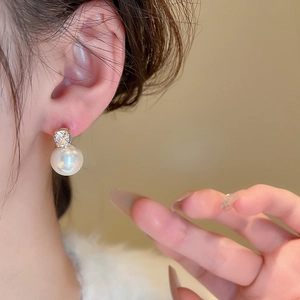 Close-up of minimalist gold earring featuring a large white pearl and sparkling zircon stud