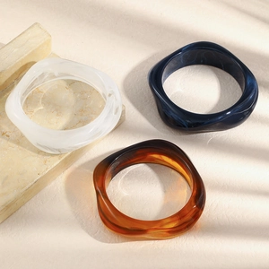 Detailed view of three acrylic geometric bangles in white, navy blue, and amber colors