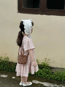 Detail shot of a pink floral toddler dress paired with a woven bucket bag and lace hat