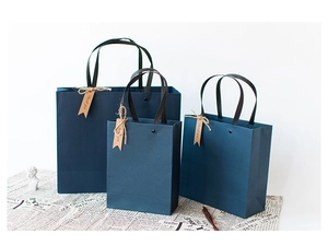 Three sizes of dark blue gift bags with black handles and thank you tags on vintage paper