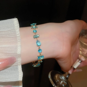 Detail of luxury gold bracelet with irregular sea blue zircons worn at a gala