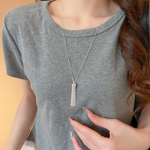 Dettaglio di una collana in argento con fiocco e lunghe nappe su maglia grigia a coste