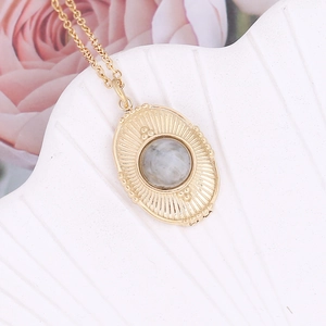 Detail of gold irregular oval pendant with grey stone and radial texture on shell tray