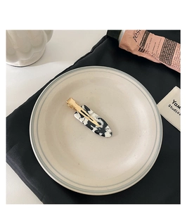 Detail of marble pattern acetate hair clip with gold metal base on ceramic plate