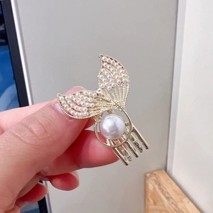 Detail of a golden fish tail hair clip with inlaid pearls held in hand for size