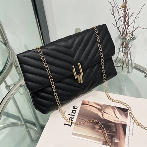 Sac bandoulière noir matelassé en V chic avec chaîne dorée sur table en verre