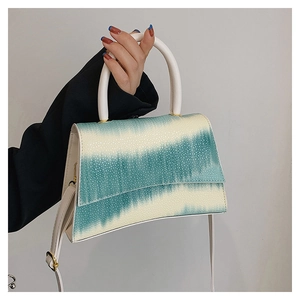 Detail of blue-green gradient handbag with grainy texture and white handle held by model