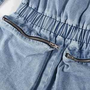 Close-up of light blue denim romper featuring elastic waist and metal zipper pockets