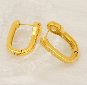 Détail de boucles d'oreilles serpent dorées avec yeux rouges et texture écaille