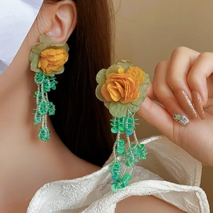 Gros plan de boucles d'oreilles fleur en tissu jaune avec glands en perles vertes