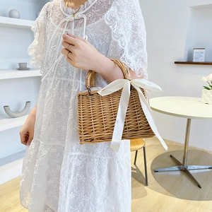 Handwoven straw basket bag featuring a large silk bow and pearls for beach vacations