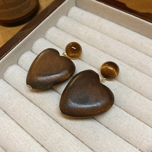 Gros plan sur des boucles d'oreilles cœur en oeil de tigre brun avec détails dorés et velours