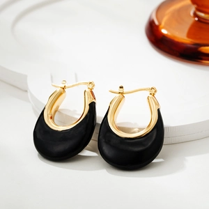 Close-up of U-shaped gold earrings with black enamel drip finish on a white stand