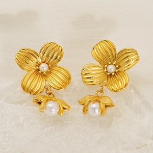 Golden flower earrings with white pearls and textured petals on a beige background