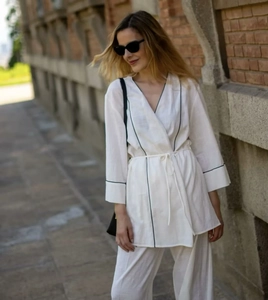 Detail eines weißen Loungewear-Tops mit V-Ausschnitt, Gürtel und dunklen Paspelierungen